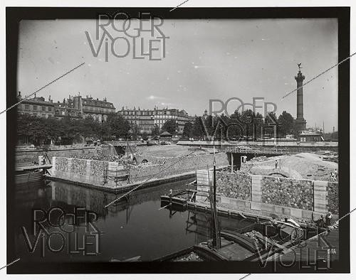 Roger-Viollet | 319082 | Construction du chemin de fer métropolitain municipal de Paris : ligne 1, 3ème lot (184). Station de la Bastille. Vue prise de la rive gauche du bassin de l'Arsenal. Paris (XIème arr.), 11 août 1899. Photographie de Charles Maindron (1861-1940). Paris, bibliothèque de l'Hôtel de Ville. | &copy; Charles Maindron / BHdV / Roger-Viollet