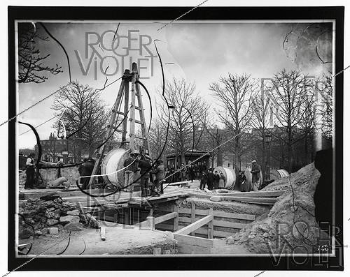 Roger-Viollet | 675017 | Construction du chemin de fer métropolitain de Paris : ligne 1, 8e lot. 458 : Souterrain à deux voies, sous la Place de l'Etoile, descente d'une bobine de câble triphasé. 13 avril 1900. Photographie de Charles Maindron (1861-1940). Paris, bibliothèque de l'Hôtel de Ville. | &copy; Charles Maindron / BHdV / Roger-Viollet