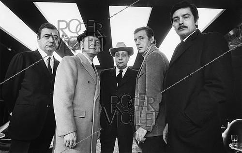 Roger-Viollet | 1375652 | Shooting of  Le Cercle rouge , film by Jean-Pierre Melville. From left to right : François Périer (1919-2002), Bourvil (1917-1970), Jean-Pierre Melville (1917-1973), Yves Montand (1921-1991) and Alain Delon (1935-2024). 1970 | &copy; André Perlstein / Roger-Viollet