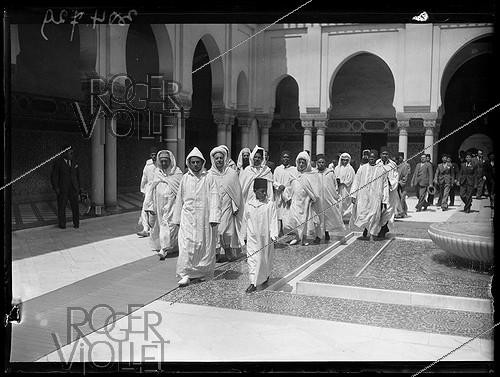 Roger-Viollet | 357617 | Visit by Mohammed V of Morocco (1909–1961), Sultan of Morocco, to the Grand Mosque of Paris with his son, Crown Prince Hassan (1929–1999), and his entourage. Behind the sultan, Si Kaddour ben Ghabrit (1868–1954) can be seen wearing a burnous; he was a high-ranking official and founder of the Muslim Institute of the Grand Mosque of Paris. Paris (5th arrondissement), June 23, 1939. Photograph from the newspaper  Excelsior.  | &copy; Excelsior - L'Equipe / Roger-Viollet